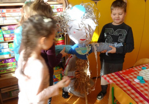 Dzieci naklejają różny materiał plastyczny na kukłę Marzanny.